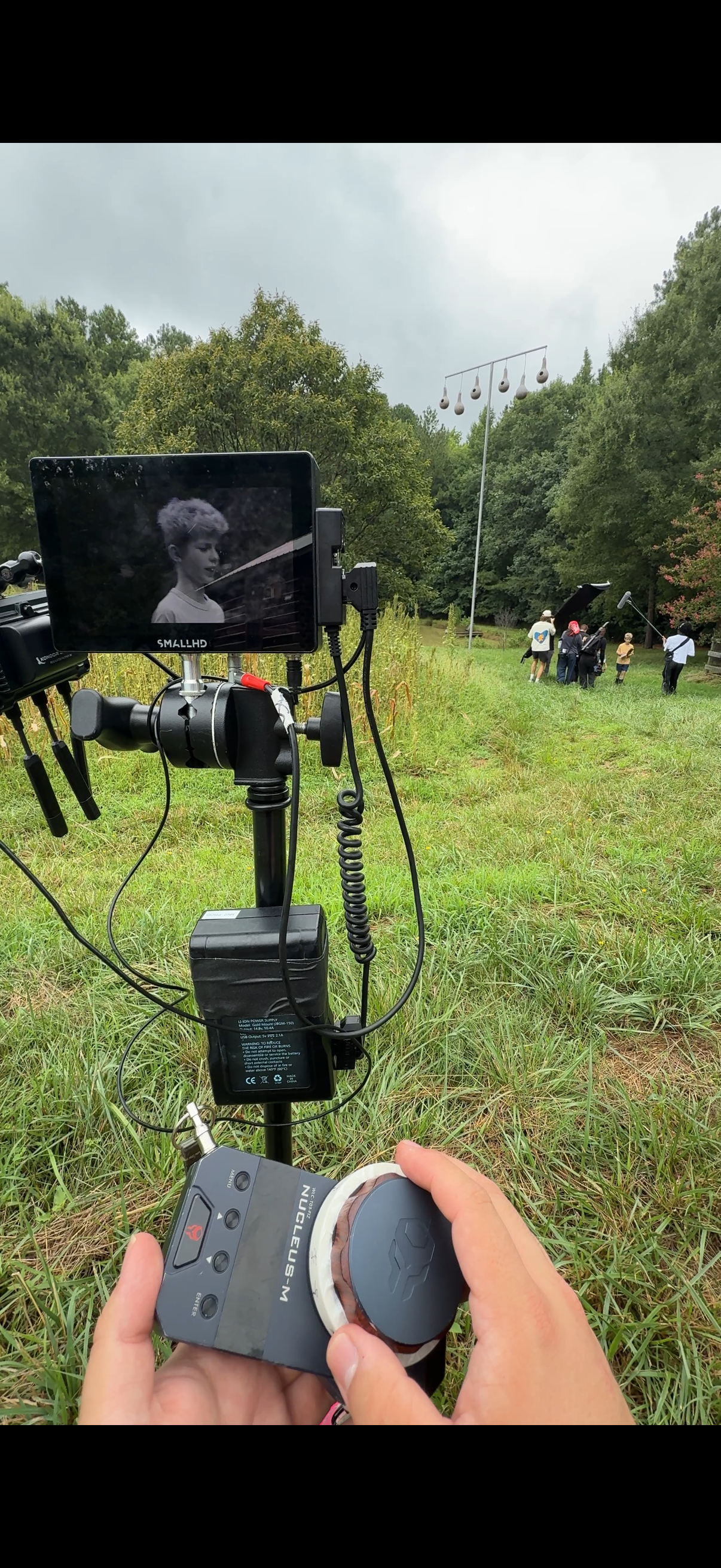 A wireless focus hand unit in the foreground, a SmallHD monitor, and a crew working on an outdoor setup.
